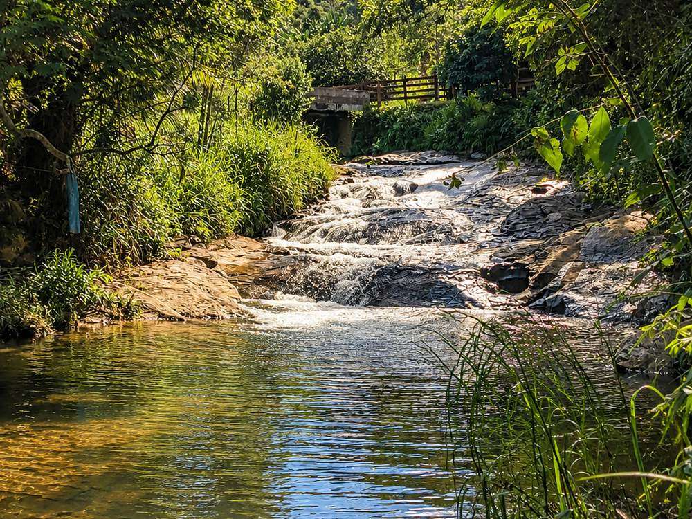 O rio do sítio: corredeira entre as pedras descendo para um poço de água clara, com a mata fechada em volta.